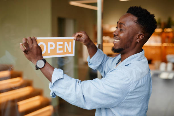 A small business owner smiles while hanging an "OPEN" sign on the door, representing crucial success tools.