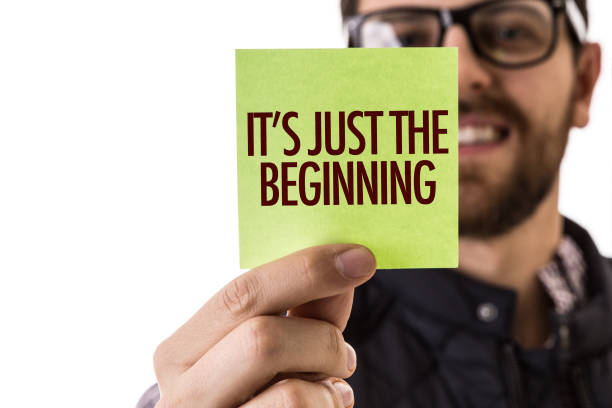 A person holds a green sticky note with the text "IT'S JUST THE BEGINNING," symbolizing a business startup.