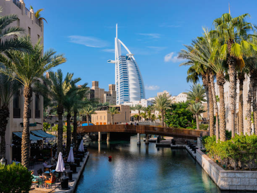 Scenic view of a modern Dubai skyscraper and a serene canal lined with palm trees, illustrating UAE free zone allure.